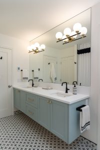 A stunning bathroom with large mirror, double sinks, vanity lighting, blue vanity cabinets and black faucets.