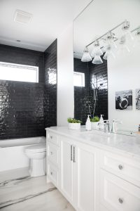 A white bathroom vanity with white countertops and black tile in the tub/shower combo.