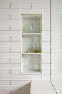 A shower with built in shelves and bench, with white subway tiles.