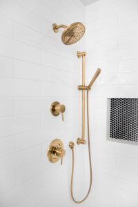 Stunning brass shower fixtures against white tile with a built-in shelf with black tile.