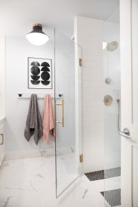 A beautiful bathroom with a glass walk-in shower, lighting, towels and artwork.