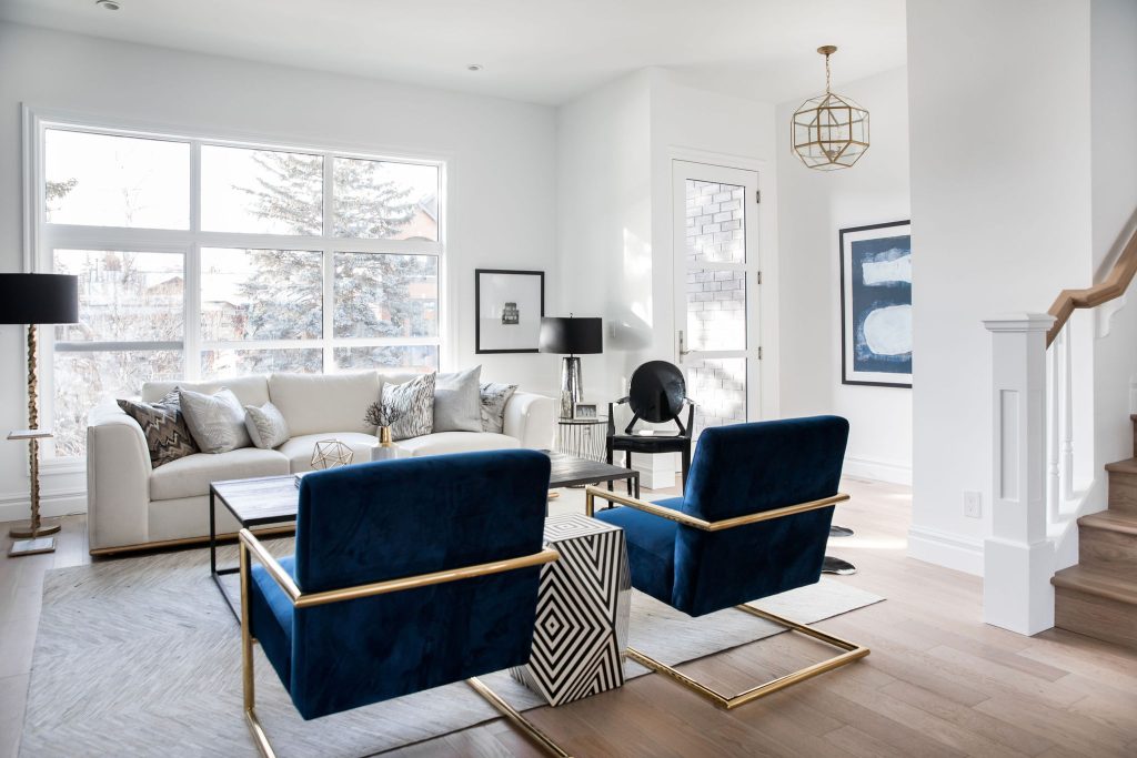 A modern bright living room with white walls, light hardwood floors, a large white sofa and royal blue chairs.