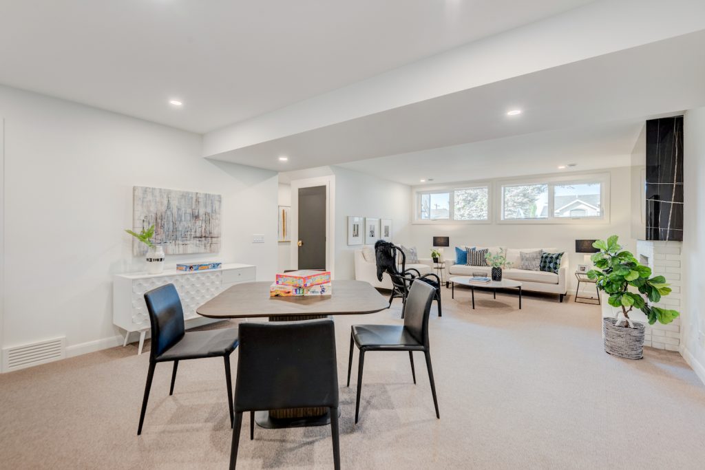 A large basement with natural lighting from windows, a living room area and dining or games table.