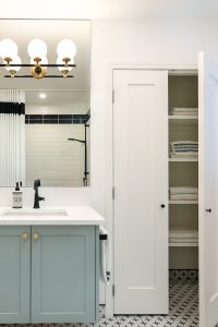 A beautiful bathroom with a linen closet, blue vanity, vanity lighting and black hardware.