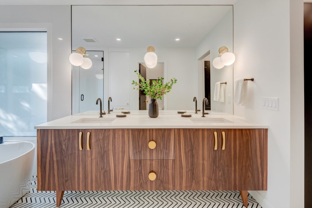 A modern bathroom vanity with light brown wood grain cabinetry and copper handles.