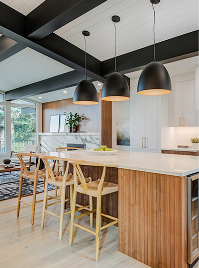 A white kitchen with wood grain cabinets, large black light fixtures over the island and large black ceiling beams.