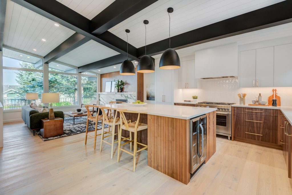 A white kitchen with wood grain cabinets, large black light fixtures over the island and large black ceiling beams.