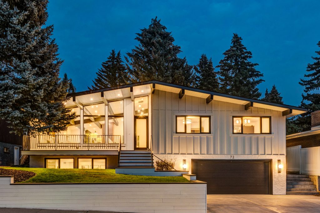 A renovated home exterior at dusk with black garage door, black roof beams, flush mount ceiling lights on a vaulted roof.