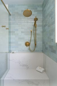 A shower with light blue tiles, brass shower hardware, and white porcelain tile.