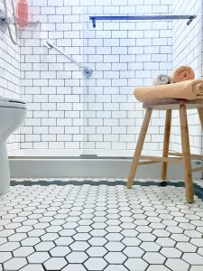 A beautiful bathroom with hexagon floor tiles, subway tile in the glass shower, and a stool with towels.