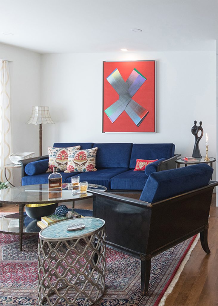 A newly renovated designer living room with a royal blue sofa and modern red painting.