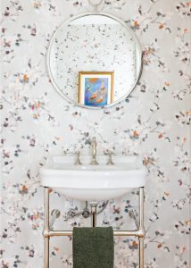 Guest bathroom with off-white flower wallpaper and round mirror.