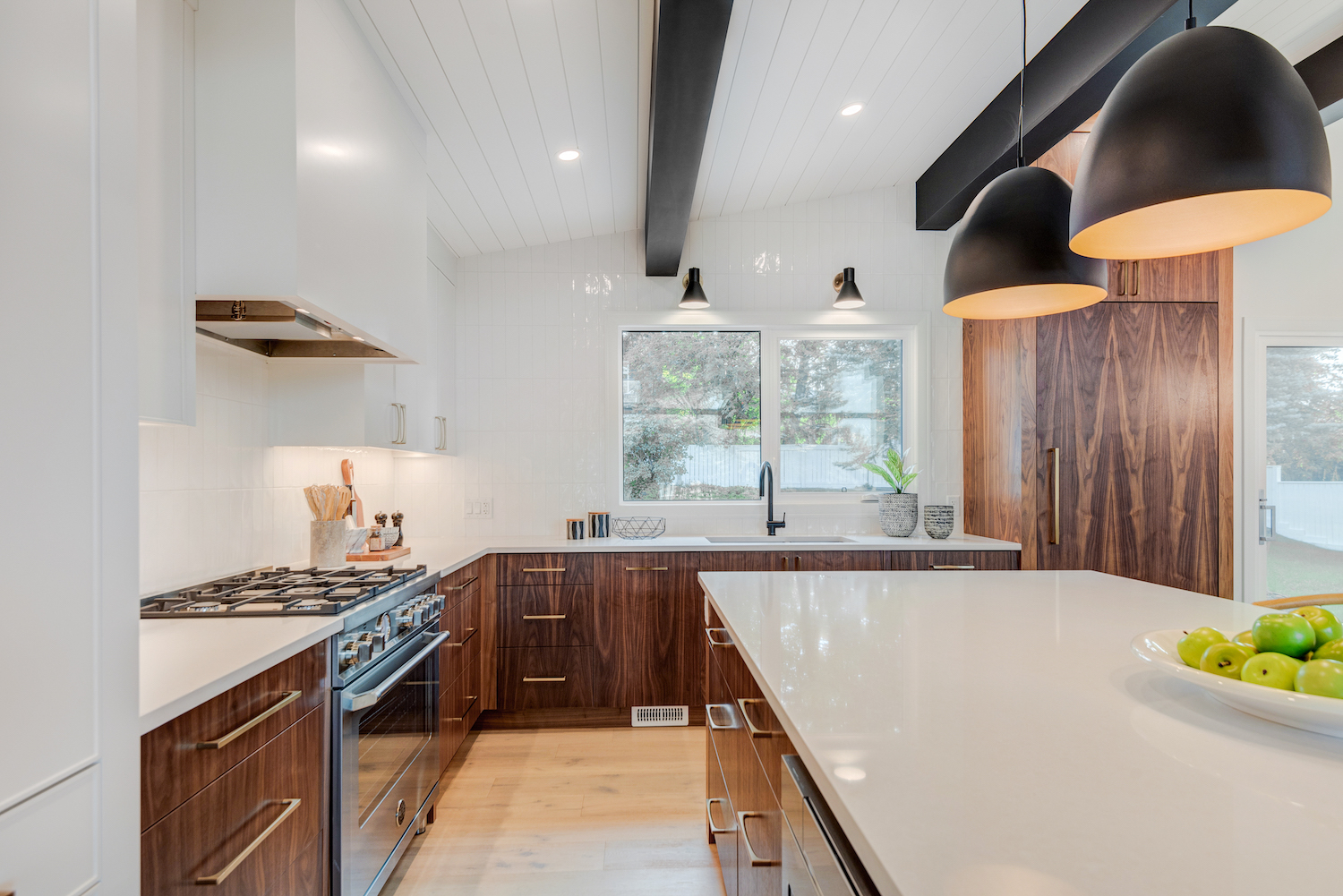 Bright and open kitchen with dark wood, white stone countertops, gold hardware and black lighting