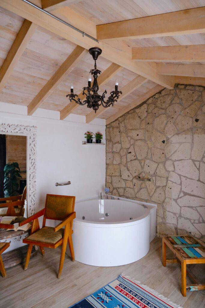 Rustic bathroom with round bathtub, wood paneling, stone walls and a black chandelier