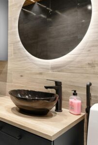 Bathroom vanity with raised black sink, black faucet, and round mirror with backlit ambient lighting