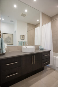 Clean and modern bathroom with dark wood vanity, round raised white sink, and beige floor and wall tiles