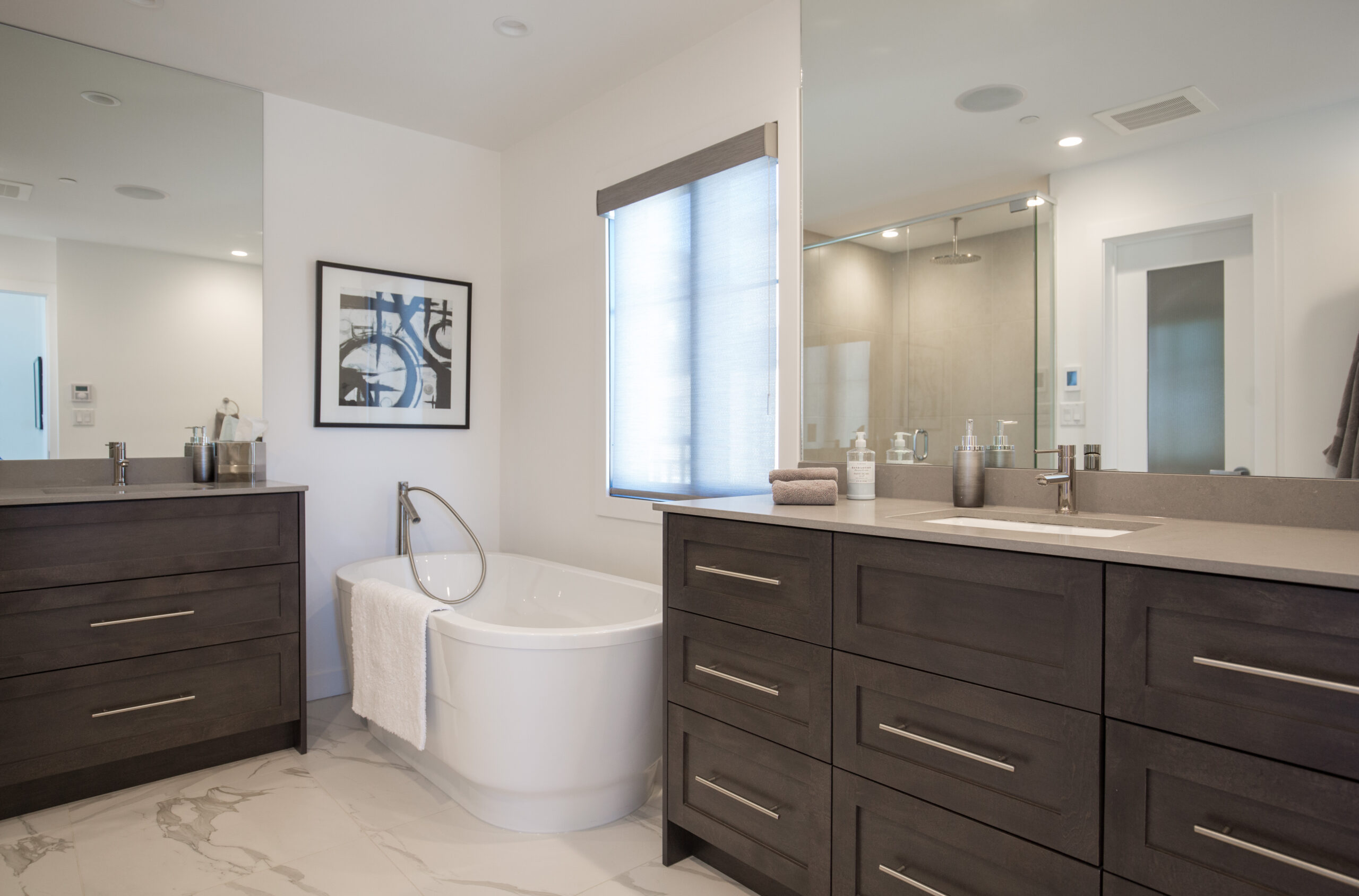 Large bathroom renovation with two dark wood vanities with large mirrors, and large corner soaker tub