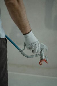 A painter's hand holding a spray wand ready to paint repaired drywall 