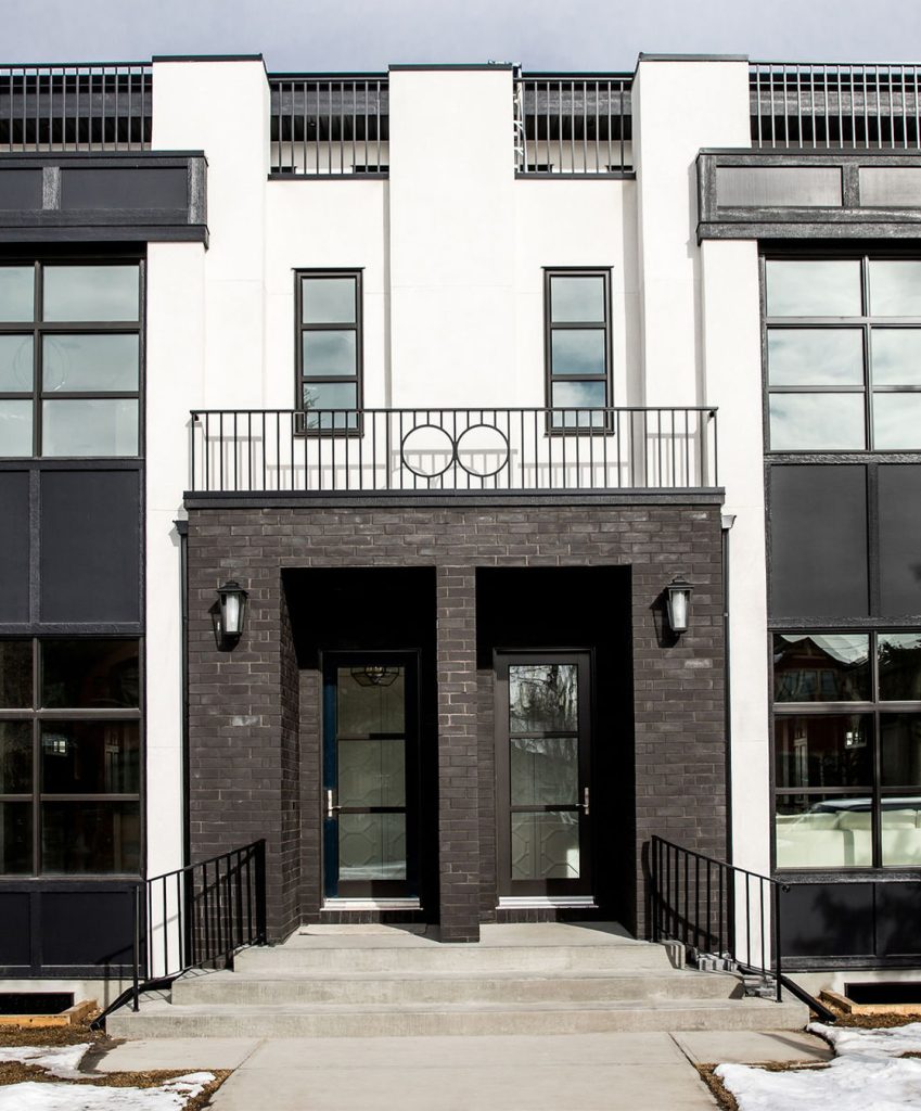 A modern white home exterior with dark brick and black panel windows.