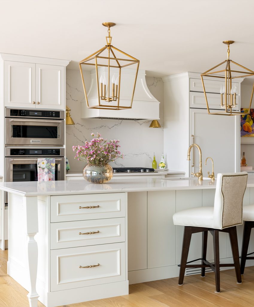 An elegant kitchen with decorative cream cabinetry and large gold feature lights.