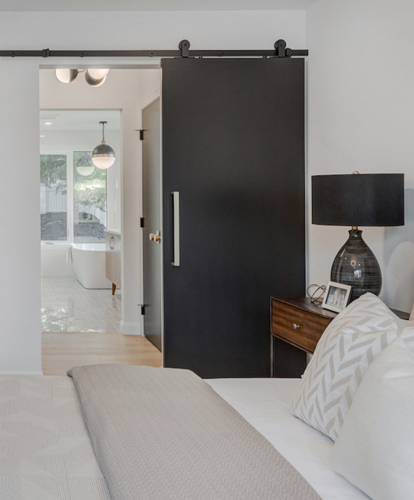 Dark brown barn door between a bathroom and a bedroom.