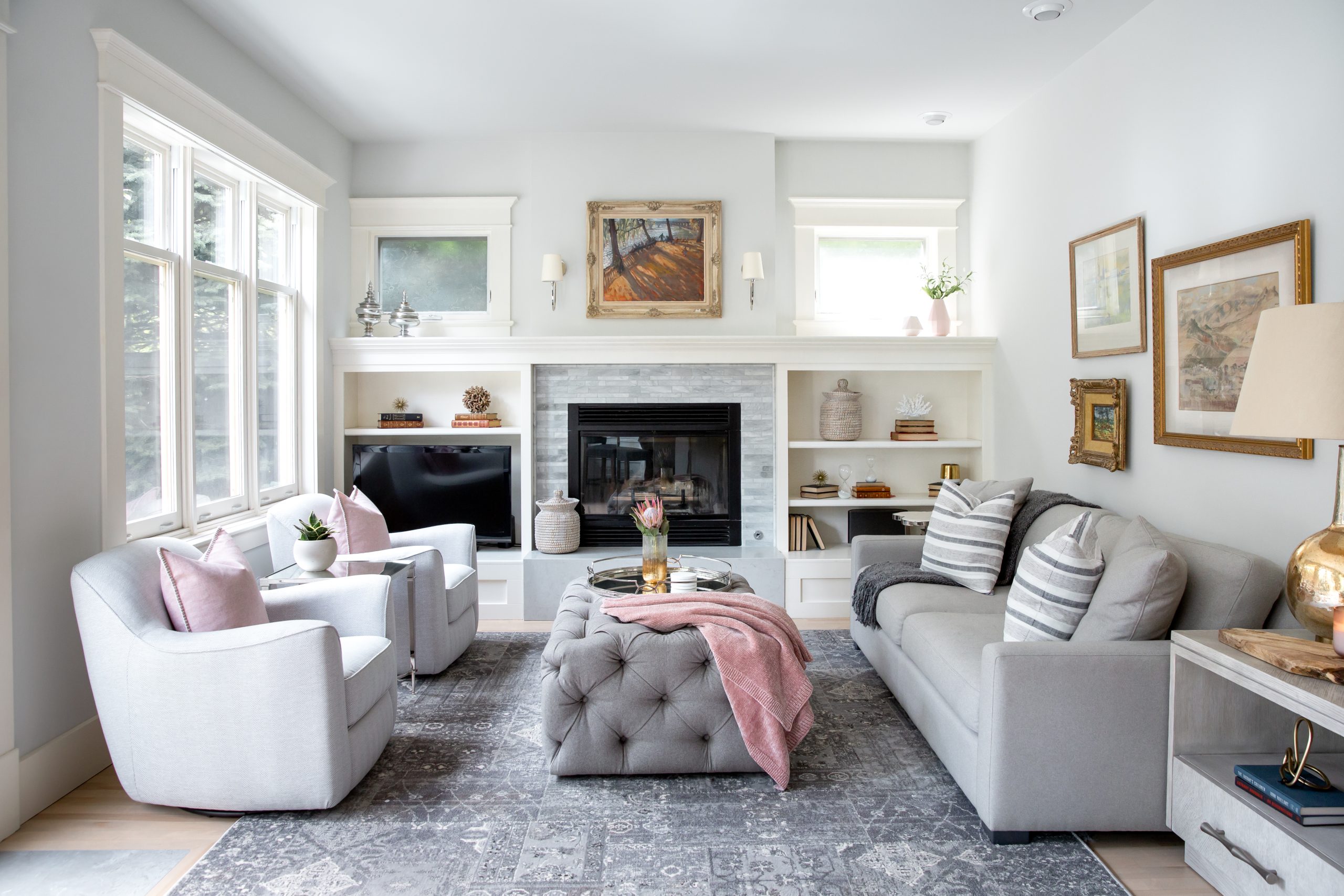 An elegant living room designed with white built-ins on either side of a fireplace and pink designer accents.