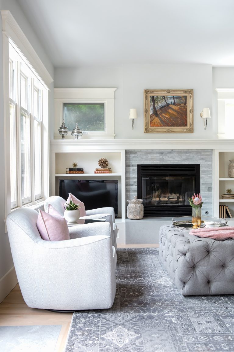 An elegant living room designed with white built-ins on either side of a fireplace and pink designer accents.